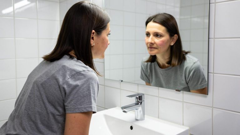 Žena se naginje nad umivaonikom i gleda odraz u ogledalu